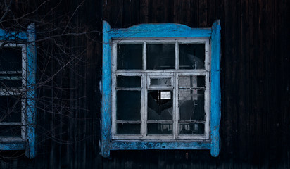 Old dark broken window with blue leaf in Russia