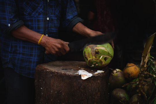 A man is cutting a fresh young green coconut with a sharp chopper or aruval for tourists