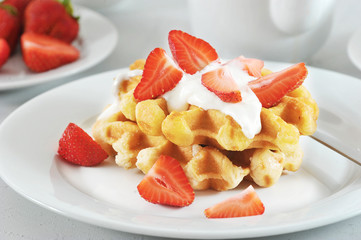 Wafers Belgian with strawberries and cream on a white plate. In the background a plate with strawberries. Light background. Close-up. Macro photography.