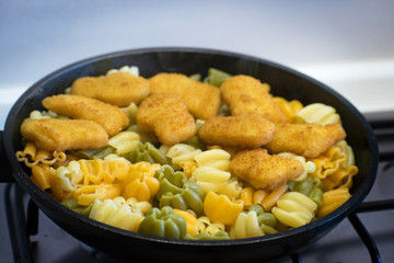 Pasta with chicken nuggets in a frying pan. Fried Chicken Nuggets. Tasty, crispy chicken nuggets. Children's menu.