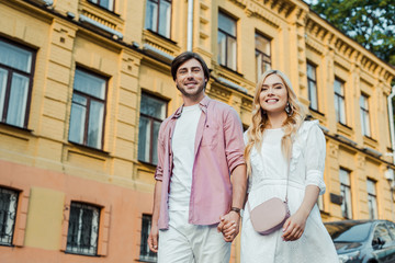 Fototapeta premium young couple holding hands while walking on city street together