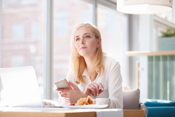Successful young woman outsourcing accountant works remotely in cafe using smartphone applications...