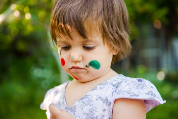 Painting. little girl is drawing. Young artist.  Funny girl  in the park.  activity for children.  funny girl painted her face. Dirty face

