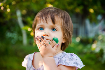 Fototapeta premium Painting. little girl is drawing. Young artist. Funny girl in the park. activity for children. funny girl painted her face. Dirty face 