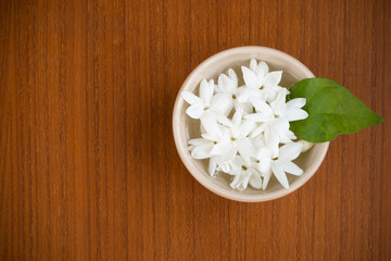 White jasmine flowers with green leaves in a small bowl with fresh new water on dark brown wooden background with copy space for text, wordings, logo insertion or decoration