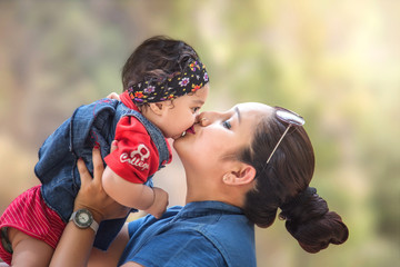 Portrait of Indian/Asian mother Kissing her cute little daughter in the park, Family outdoor lifestyle.