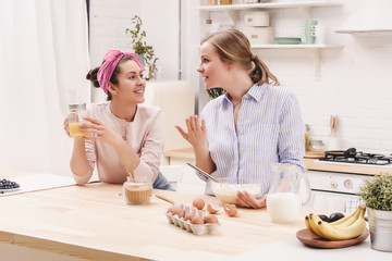 Two cheerful friends cook together desserts and gossip in the kitchen
