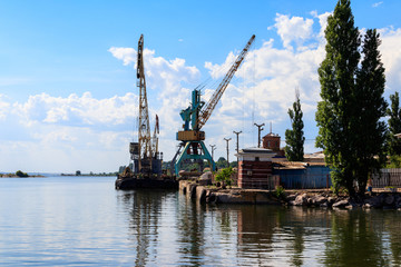 Fototapeta na wymiar Heavy cranes in cargo port on the riverbank
