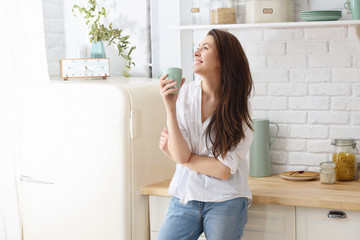 Young happy woman drinking coffee on the kitchen in the morning - Powered by Adobe