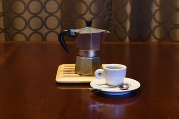 Moka stove-top espresso coffee maker with cups and spoons in a variety of dramatic lighting on a wooden table at night.