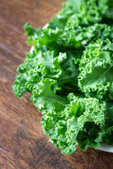 Kale. Green vegetable leaves on plate on wooden background. Healthy eating, vegetarian food.