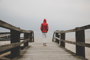 Woman in red jacket standing on the wooden pier, back view