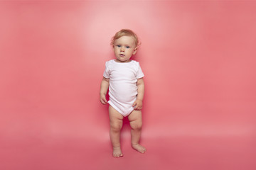one year old girl with curly hair in white clothes in full growth on a pink background. concept of childcare.