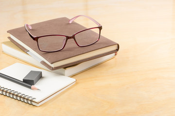 eyeglasses with books and stationary on wooden table, copy space for text. business and education concept.