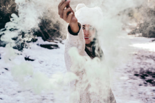.Young and relaxed woman enjoying a sunny winter day in the mountains. Surrounded by snow and trunks holding a tube of green smoke, funny photo. Lifesytle