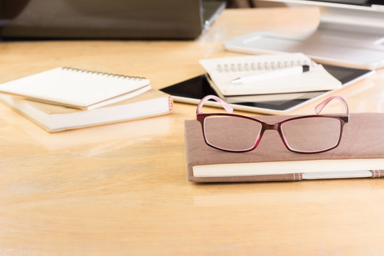 eyeglasses on a book with office tools on wooden table, copy space. business and education concept.