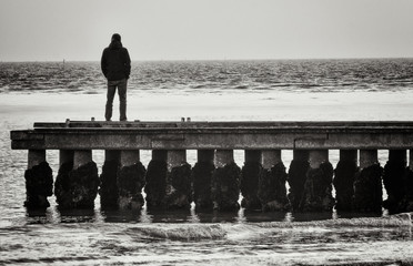 Lonely man standing on a pier staring at the sea