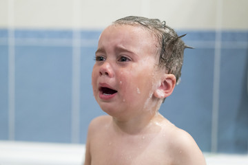 Crying baby by in a bathtub. Infant kid sreaming while taking a bath. baby cries in the bathroom
