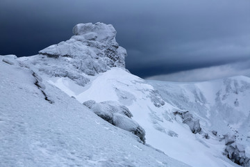 Mysterious fantastic rocks frozen with ice and snow of strange fairytales forms and structures. Nice view from the lawn to the mountains in snow, interesting light and fog.