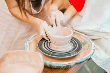 Women working on the potter's wheel. Hands sculpts a cup from clay pot. Workshop on modeling on the potter's wheel.