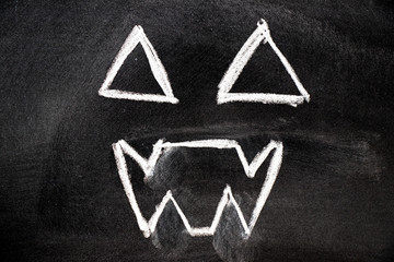 White color chalk hand drawing in ghost face shape on blackboard background