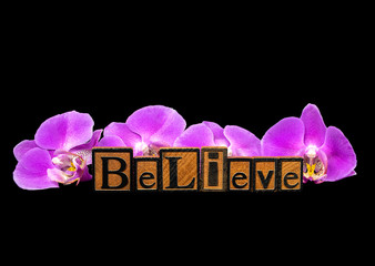 word believe in vintage wooden letterpress typeset with pink orchids on black