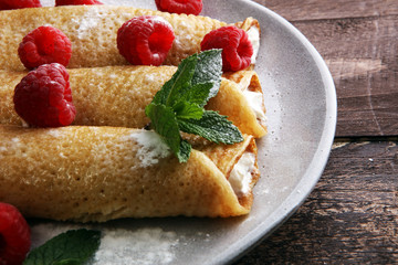 Homemade crepes served with fresh raspberrries and powdered sugar on rustic wooden table