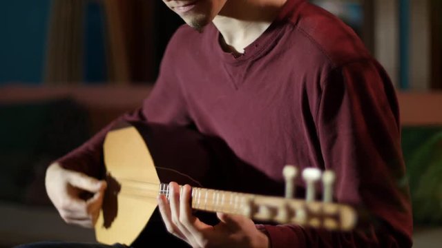 Closeup on the fingering on a beautifully lit saz being performed by a young man.
