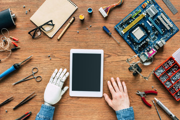 cropped image of  electronic engineer with robotic hand sittng at table with digital tablet...