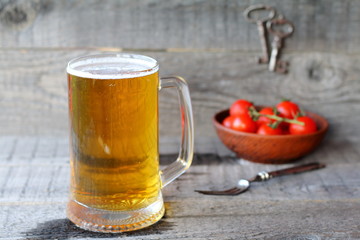 A mug of  light beer and fresh tomatoes in a clay bowl on a wooden background.
