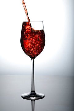 cherry red wine being poured in tall wine glass with splash and bubbles