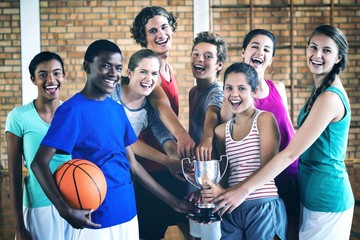 Smiling high school kids holding trophy in basketball court