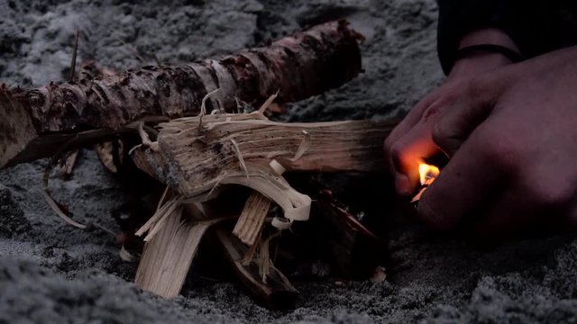 Person setting fire to wood to make a fireplace on sand