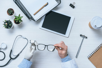 cropped image of male doctor with prosthetic arm holding eyeglasses at table with blank digital tablet