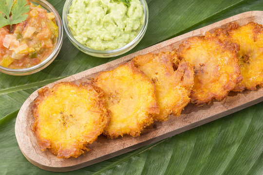 Patacon or toston fried and flattened pieces of green plantain, traditional snack or accompaniment in the Caribbean, guacamole and tomato onion salad beside, photographed overhead with natural light