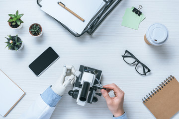 cropped shot of male scientist with prosthetic arm using microscope at table