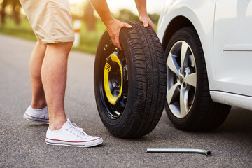 The man changes the tire to a broken car