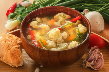Vegetable soup of cauliflower, carrots, tomato, pepper in a plate with bread and onions on a wooden background. Close-up