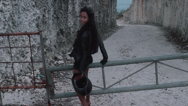 Beautiful happy woman motorcycle rider walking with helmet near amazing limestone cliffs. Girl getting over stile and gesturing come along follow me - video in slow motion