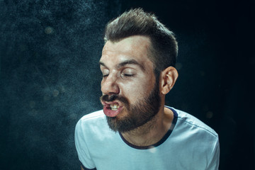 Young handsome man with beard sneezing, studio portrait