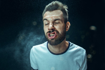 Young handsome man with beard sneezing, studio portrait