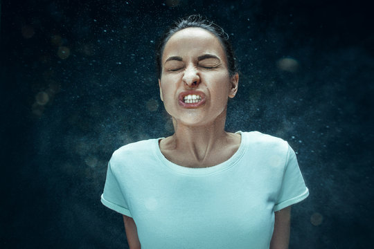 Young woman sneezing, studio portrait
