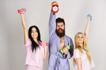Fitness morning concept. Cheerful friends with dumbbells in domestic clothes, grey background....