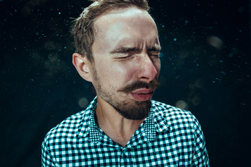 Young handsome man with beard sneezing, studio portrait