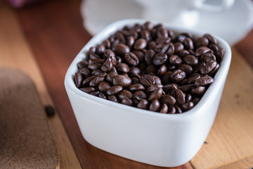 Coffee beans in white bowl on wooden table