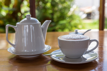 Cappuccino cup with tea pot on wooden table
