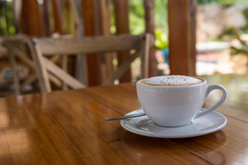 Cappuccino cup on wooden table with wooden chairs