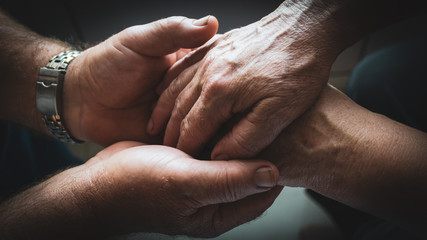 An elderly man is holding the hands of his elderly wife in his strong, laboring palms. Elderly couple love each other despite age
