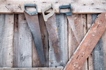 Three old rusty saws hanging on the wooden wall