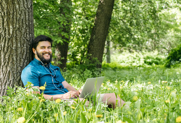 Naklejka na ściany i meble Young modern businessman freelancer working on computer and sitting on grass